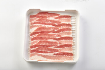 Freshly sliced raw pork belly arranged neatly in white plastic tray, showcasing its marbled texture...