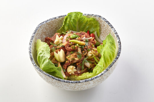 Bowl of spicy raw chopped beef salad garnished with fresh herbs, garlic, and vegetables, served on bed of crisp lettuce leaves in ceramic bowl, showcasing vibrant colors and textures