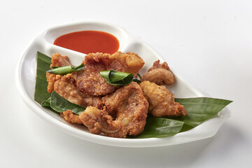 Crispy fried chicken skin served on white plate with banana leaves and side of spicy dipping sauce, creating delicious and crunchy snack presentation
