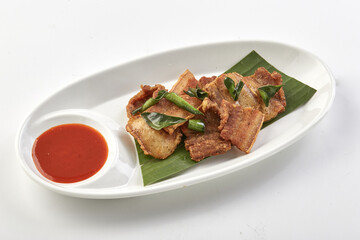 Crispy fried pork belly served on banana leaf with side of spicy red dipping sauce, presented on...