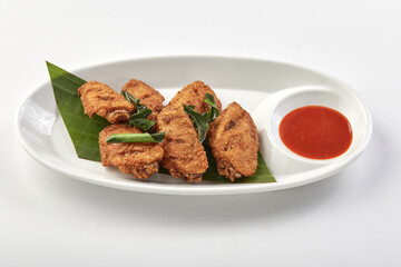 Crispy fried chicken wings served on white plate with banana leaf garnish and side of red dipping sauce, creating delicious and appetizing presentation
