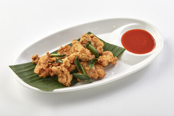 Crispy fried chicken skin served on banana leaf with side of spicy red dipping sauce, presented on white oval plate for delicious and appetizing snack