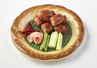 Traditional Thai Isaan sausage served on banana leaf with fresh cucumber, long beans, pickled ginger, and dried chili, presented on decorative ceramic plate