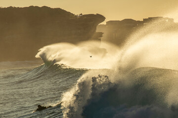 Powerful waves crash at Bronte Beach, Sydney, captured during golden light as sea spray dances in...