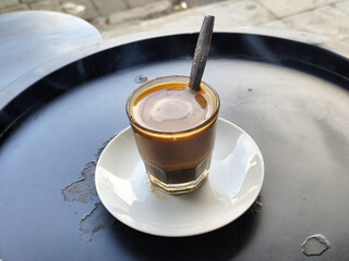 This close-up photo shows a cup of hot black coffee served on a small white plate with a spoon...