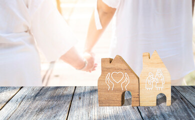 Nursing home service concept, miniature house on wood floor over blurred girl holding hand crossing the bridge, health care and elderly care