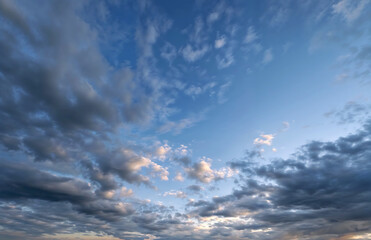 Beautiful wide-angle view of vibrant blue sky with scattered fluffy white and gray clouds at sunset or sunrise, creating dramatic atmospheric backdrop