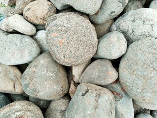 close-up texture of a pile of river rocks that have round or oval shapes with various sizes and...