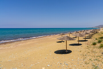 Straw sun umbrellas on an empty sandy beach overlooking deep blue Sea in southern Cyprus....