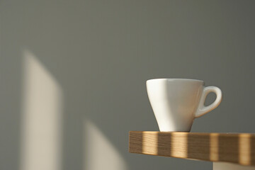 White coffee cup on wooden table under morning window light on clean grey wall background.