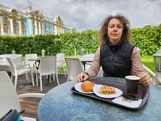 Woman is sitting at a table with a tray of food in front of her. She is wearing a black jacket and...