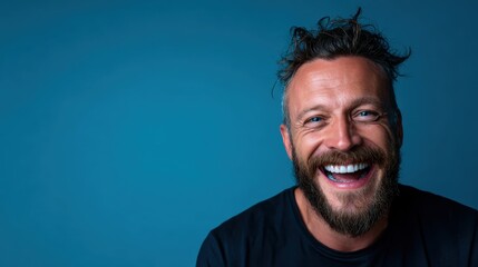 Fototapeta premium A joyful man with a beard is smiling widely against a bright blue backdrop, capturing a moment of genuine happiness and positivity that resonates with viewers.