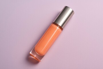 An orange lip gloss with silver cap on a light purple background view