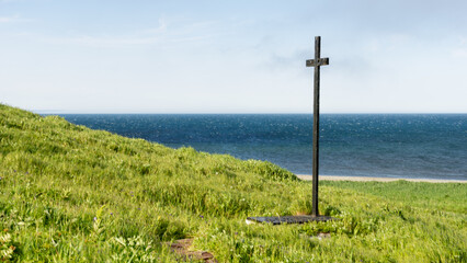Cross standing on a grassy hill overlooking a serene ocean view, symbolizing peace and reflection...
