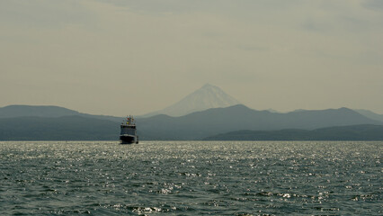 Boat sailing on calm waters with shimmering reflections, surrounded by distant mountains and a...
