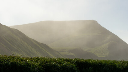 Lush green hills shrouded in mist, showcasing the beauty of nature's landscape, with rolling slopes...