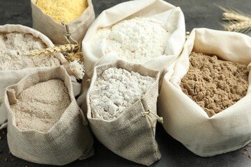 Different types of flour in bags on grey table, closeup