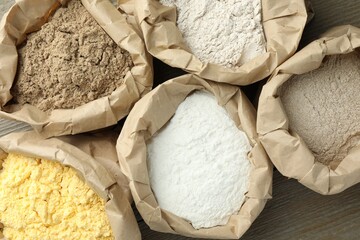 Different types of flour in paper bags on wooden table, flat lay