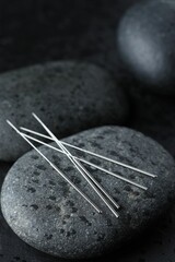 Acupuncture needles and wet spa stones on dark background, closeup