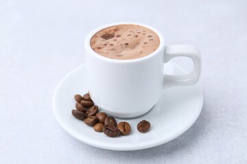 Aromatic coffee in cup, beans and saucer on light table, closeup