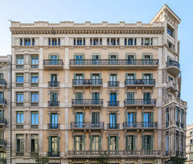 Obraz premium Grand Historic Residential Building Facade In Barcelona With Ornate Balconies And Detailed Stone Work. Traditional Spanish Architecture, Urban Landmark, Architectural Heritage