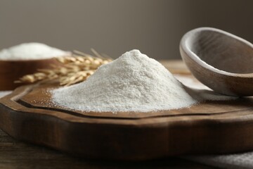 Wheat flour, spikelets and spoon on wooden table, closeup