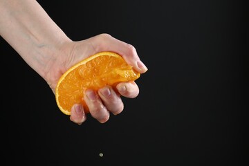 Woman squeezing orange on black background, closeup. Space for text