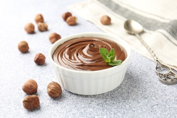 Tasty chocolate spread with mint in bowl and hazelnuts on grey textured table, closeup