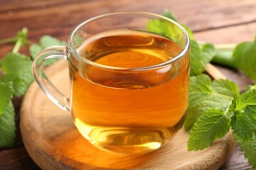 Aromatic lemon balm tea in glass cup and fresh leaves on table, closeup