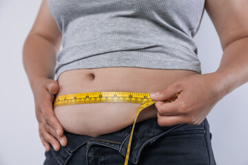 Overweight woman measuring her belly with tape on light background, closeup