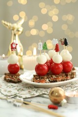 Tasty canapes and Christmas decor on white marble table against background with blurred lights, closeup. Bokeh effect