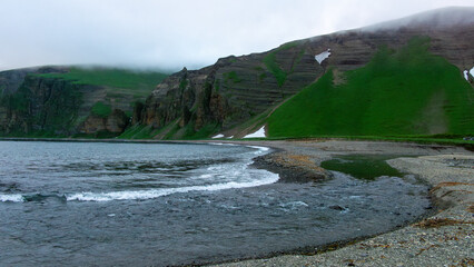 Serene coastal landscape featuring gentle waves lapping against a rocky shore, with lush green hills rising dramatically in the background, creating a tranquil natural scene