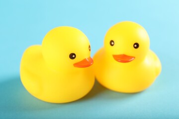 Two cute rubber ducks on light blue background, closeup