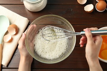 Woman whisking egg whites in bowl at wooden table, top view
