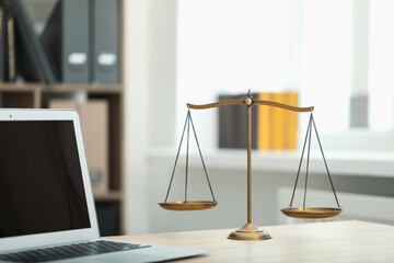 Judge's workplace with laptop and scales on wooden table in office, closeup