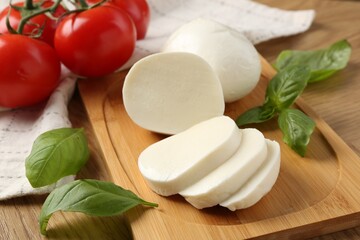 Tasty mozzarella, tomatoes and basil on wooden table, closeup