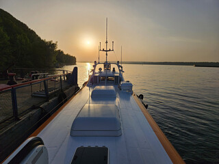 Boat hydrofoil ship is on the water with a sunset in the background. The boat is white and has a...