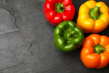 Fresh colorful bell peppers on black textured table, flat lay. Space for text
