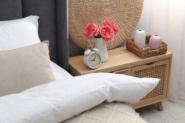 Bedside table with alarm clock and decor near bed indoors