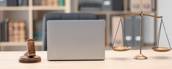 Judge's gavel, scales and laptop on wooden table in office