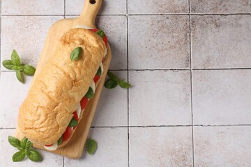 Tasty sandwich with mozzarella cheese, tomatoes and basil on light tiled table, flat lay. Space for...
