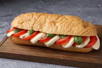 Tasty sandwich with mozzarella cheese, tomatoes and basil on grey textured table, closeup