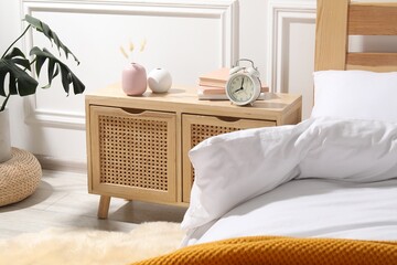 Bedside table with alarm clock, books and decor near bed indoors © New Africa