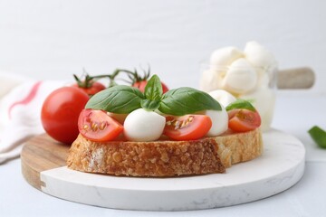 Tasty sandwich with mozzarella cheese, tomatoes and basil on light table, closeup