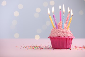 Burning candles in cupcake and sprinkles on table against blurred lights. Space for text