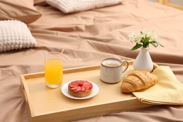 Tray with delicious breakfast and flowers on bed indoors. Space for text