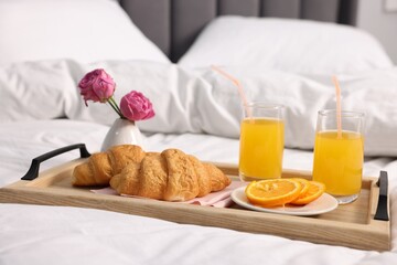 Tray with delicious breakfast and flowers on bed indoors, closeup
