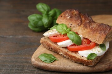 Tasty sandwich with mozzarella cheese, tomatoes and basil on wooden table, closeup. Space for text