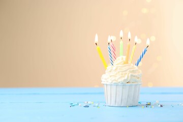 Burning candles in cupcake and sprinkles on light blue table against beige background with blurred...