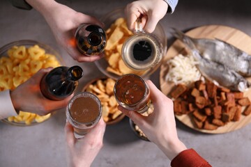 Friends clinking glasses of beer at grey table, top view